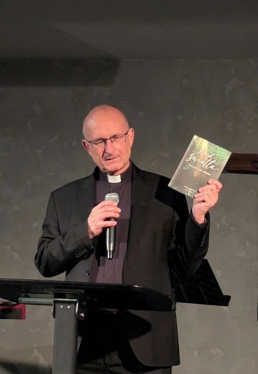 A speaker at the lectern holding the Polish edition of the book